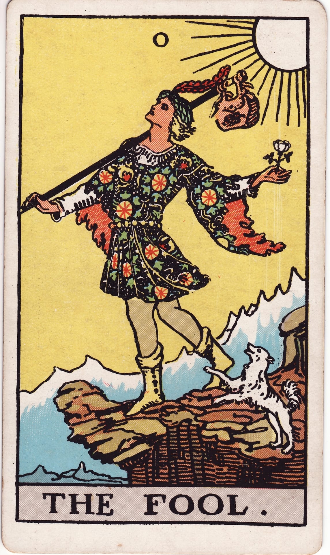 The fool card with a man standing on a cliff about to begin a journey with a small dog near his feet